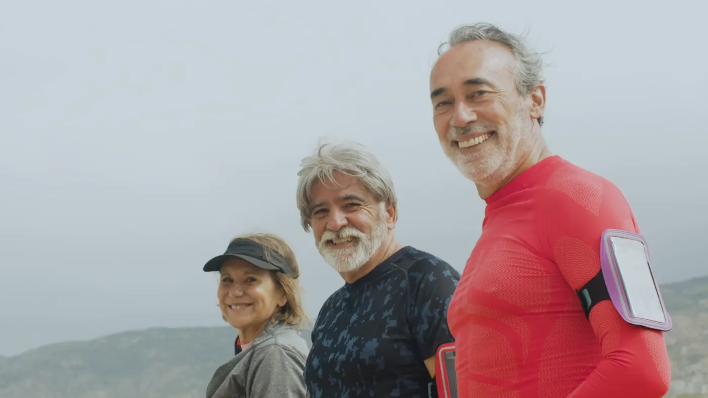 Three smiling older adults in sportswear standing together outdoors after a workout