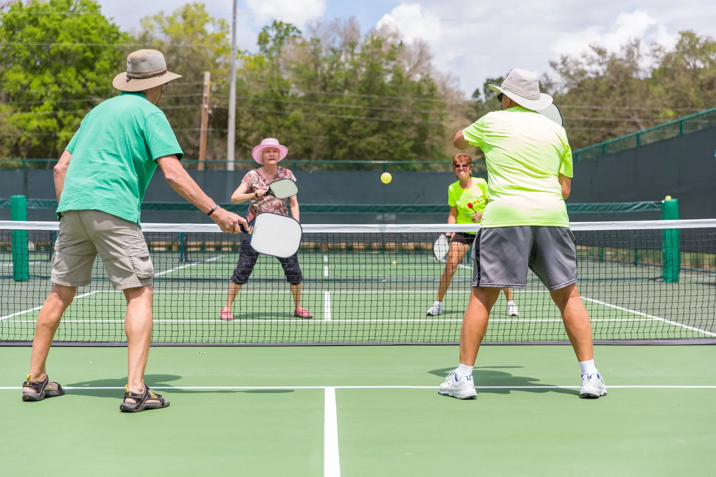Older adults in sun hats playing a friendly doubles game of pickleball on an outdoor court